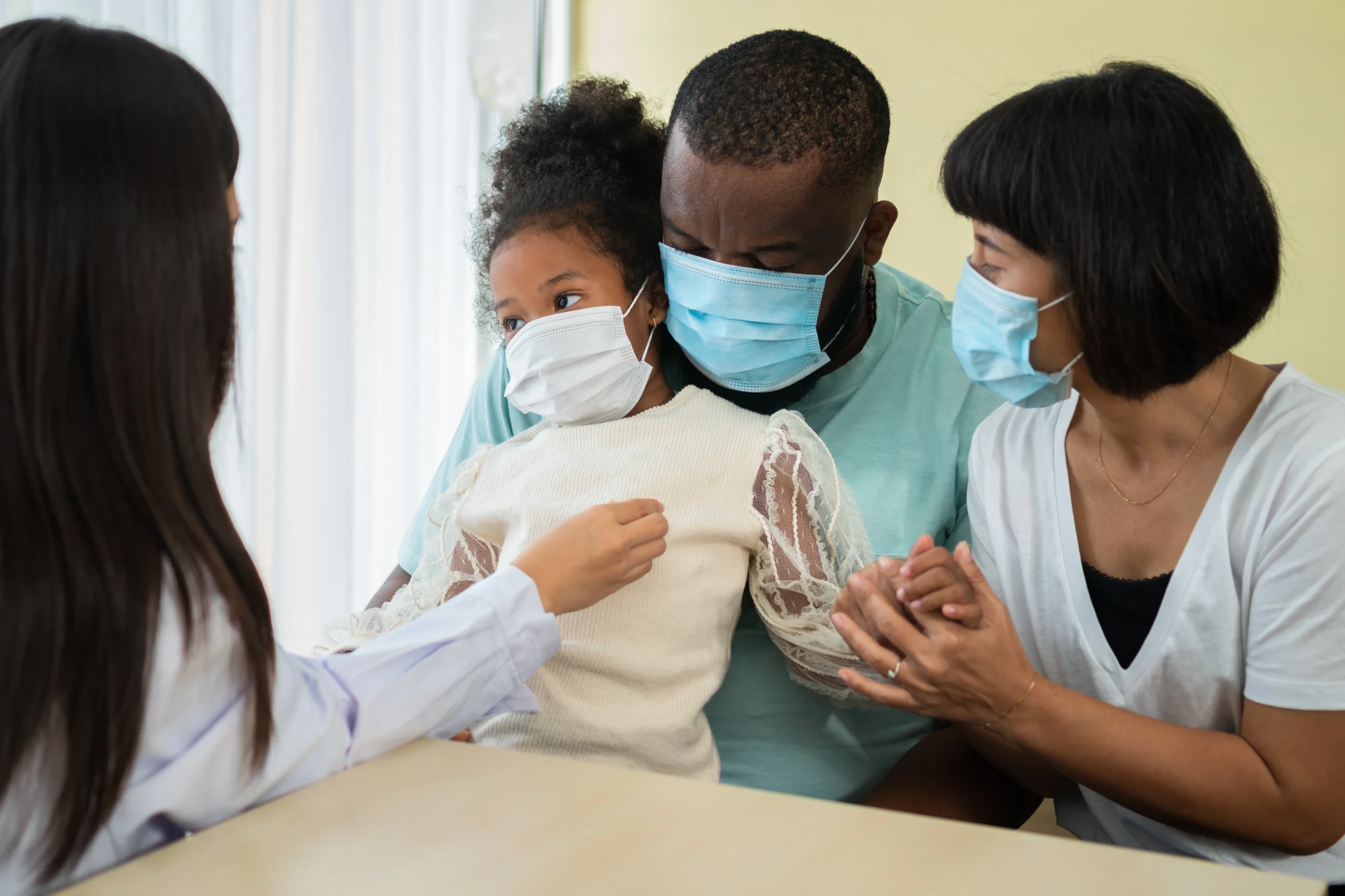 A young BIPOC girl getting a checkup from a pediatrician with her father and mother present