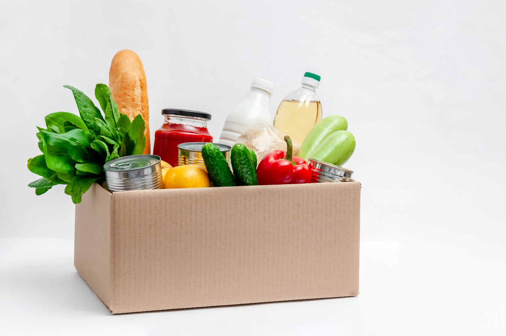 A box filled with items from a food pantry, including milk, fresh vegetables, canned goods, and bread